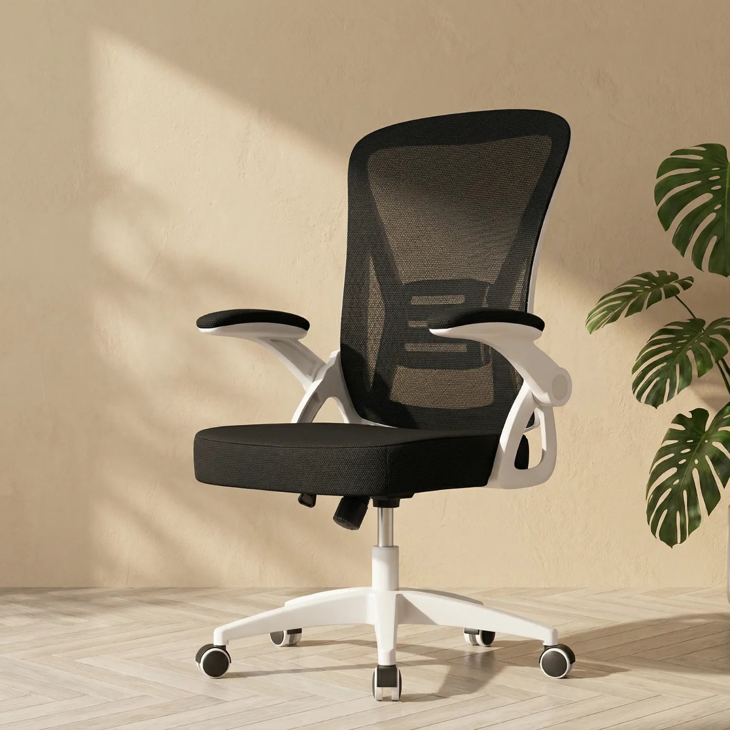 District 12 chaise de bureau ergonomique mesh noire cadre blanc, accoudoirs 90 degrés relevables, décor intérieur avec plante monstera fond beige texturé