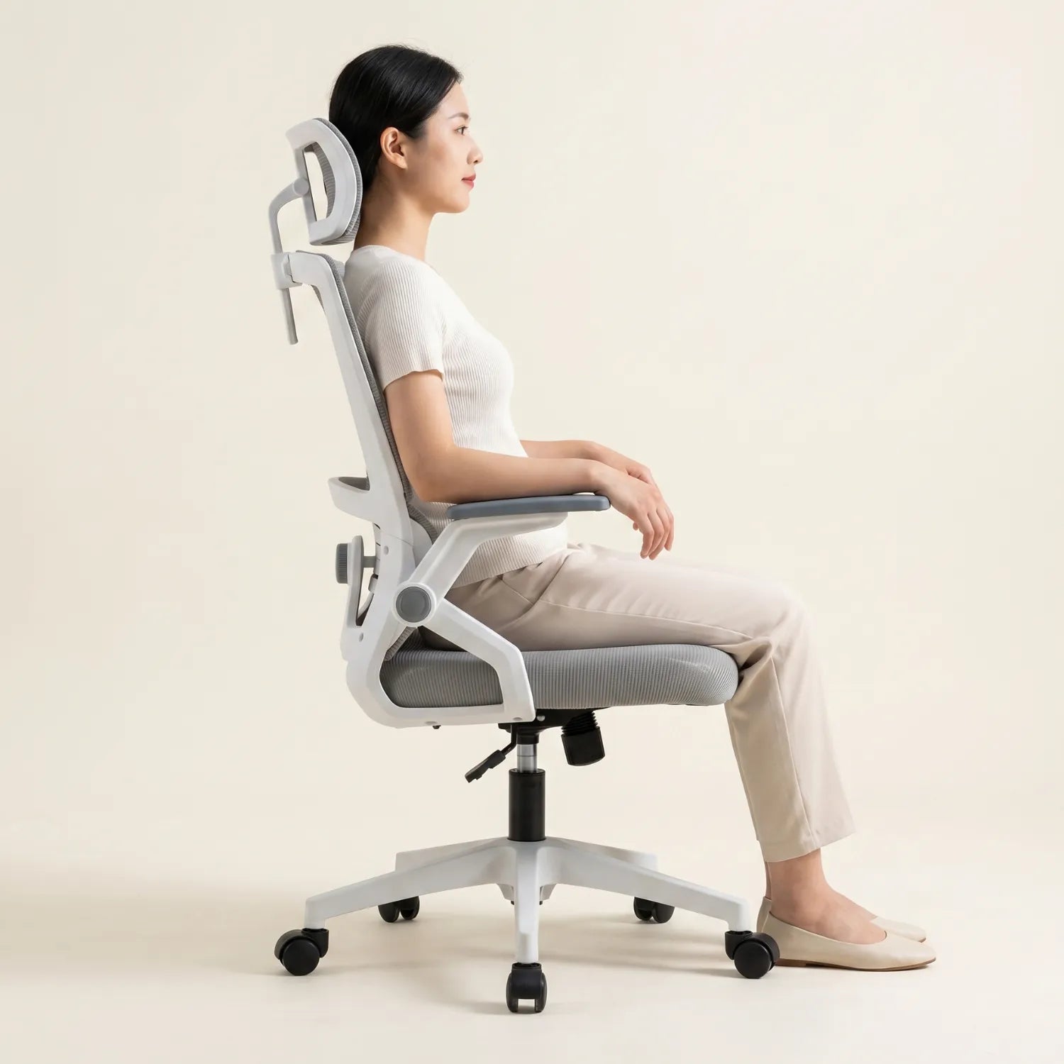 Femme assise de profil en posture ergonomique correcte sur la District 17 chaise bureau maille respirante appui-tête réglable, fond neutre studio crème