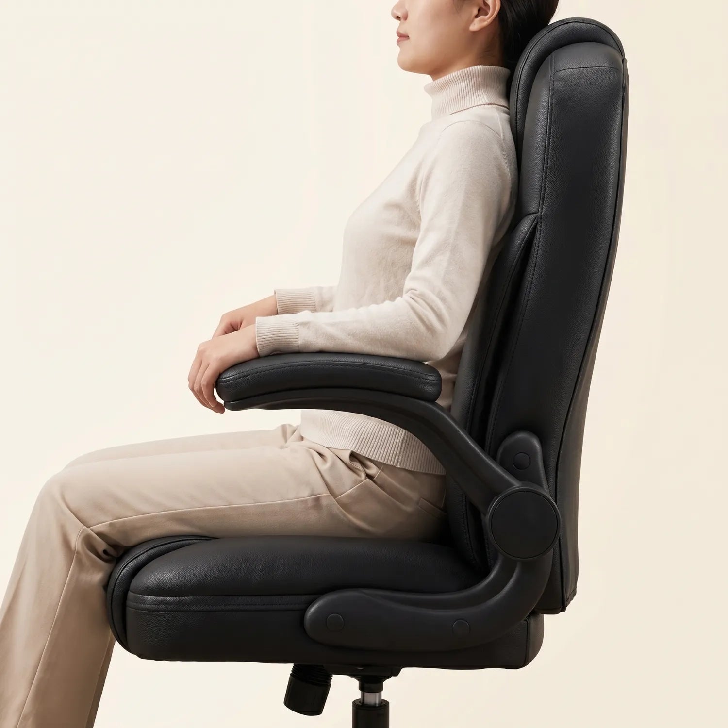 Femme assise de profil en posture ergonomique sur la District 19 chaise bureau cuir noir élite accoudoirs rabattables, soutien lombaire intégré fond neutre studio