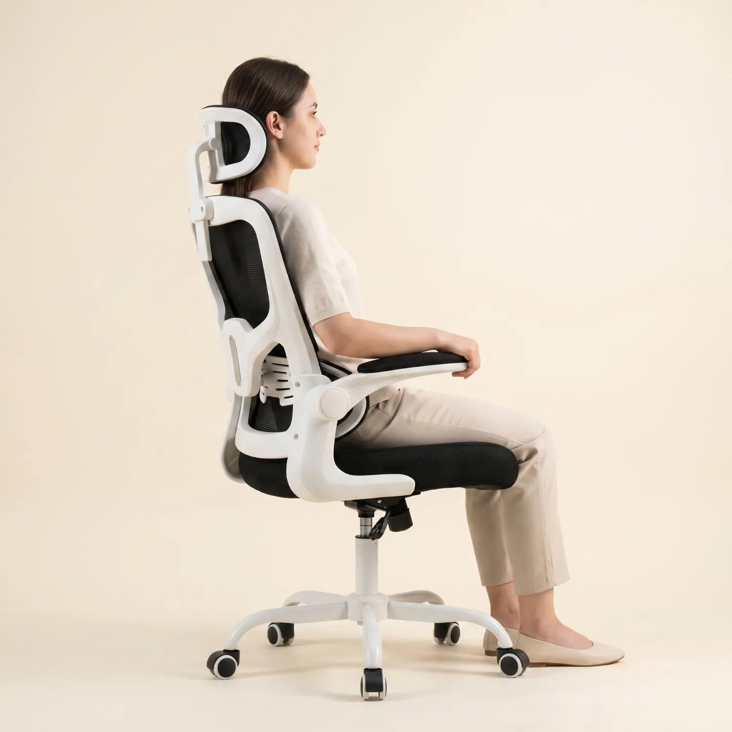 Femme assise de profil en posture ergonomique correcte sur la District 22 chaise bureau maille 3 segments noir blanc avec appui-tête réglable, fond studio crème